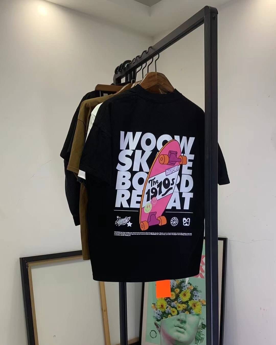 Unisex oversized black T-shirt with colorful skateboard graphic print on the back, hanging on a clothing rack.